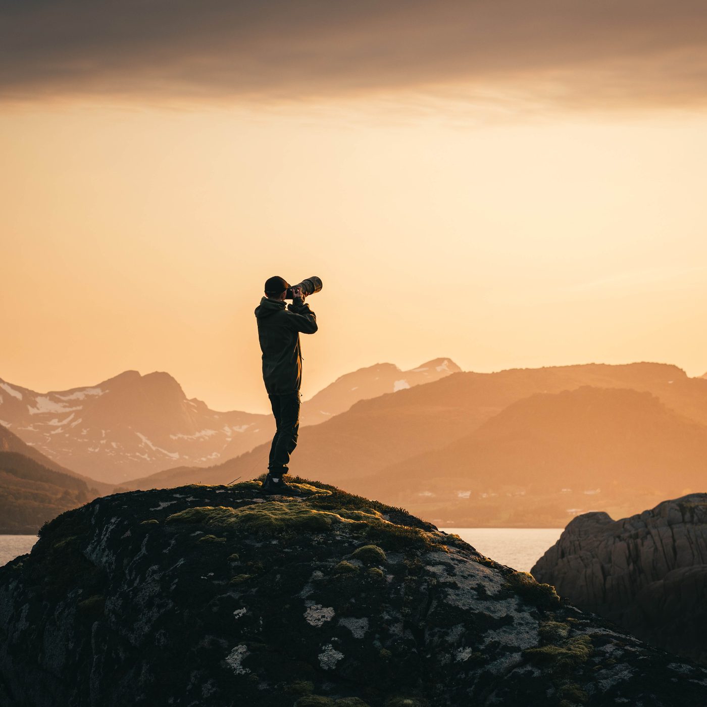 Jan with a long lens on a rock at sunset, mountains behind