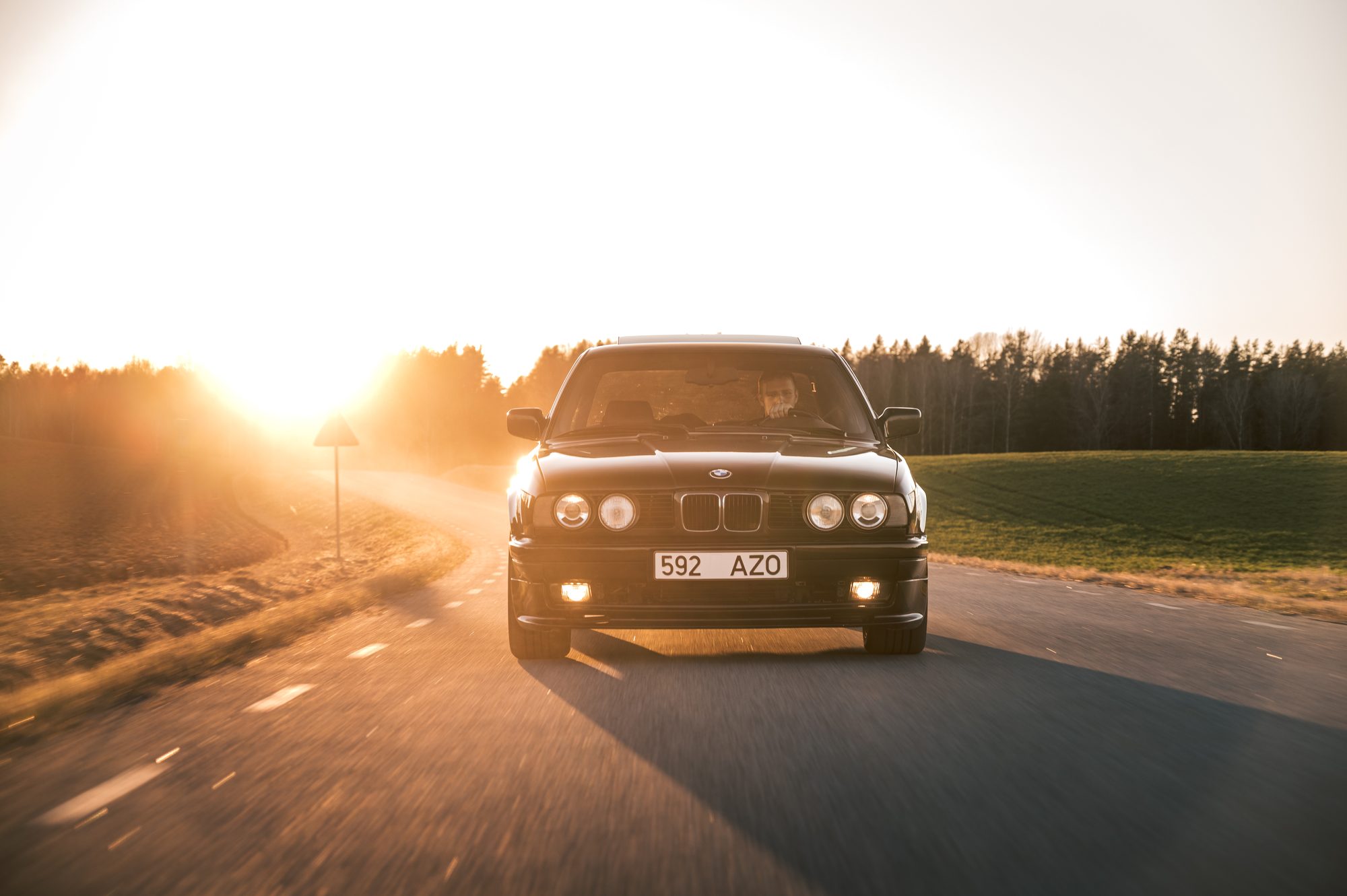 Black BMW E34 on a country road, low sun behind it and dust in the air