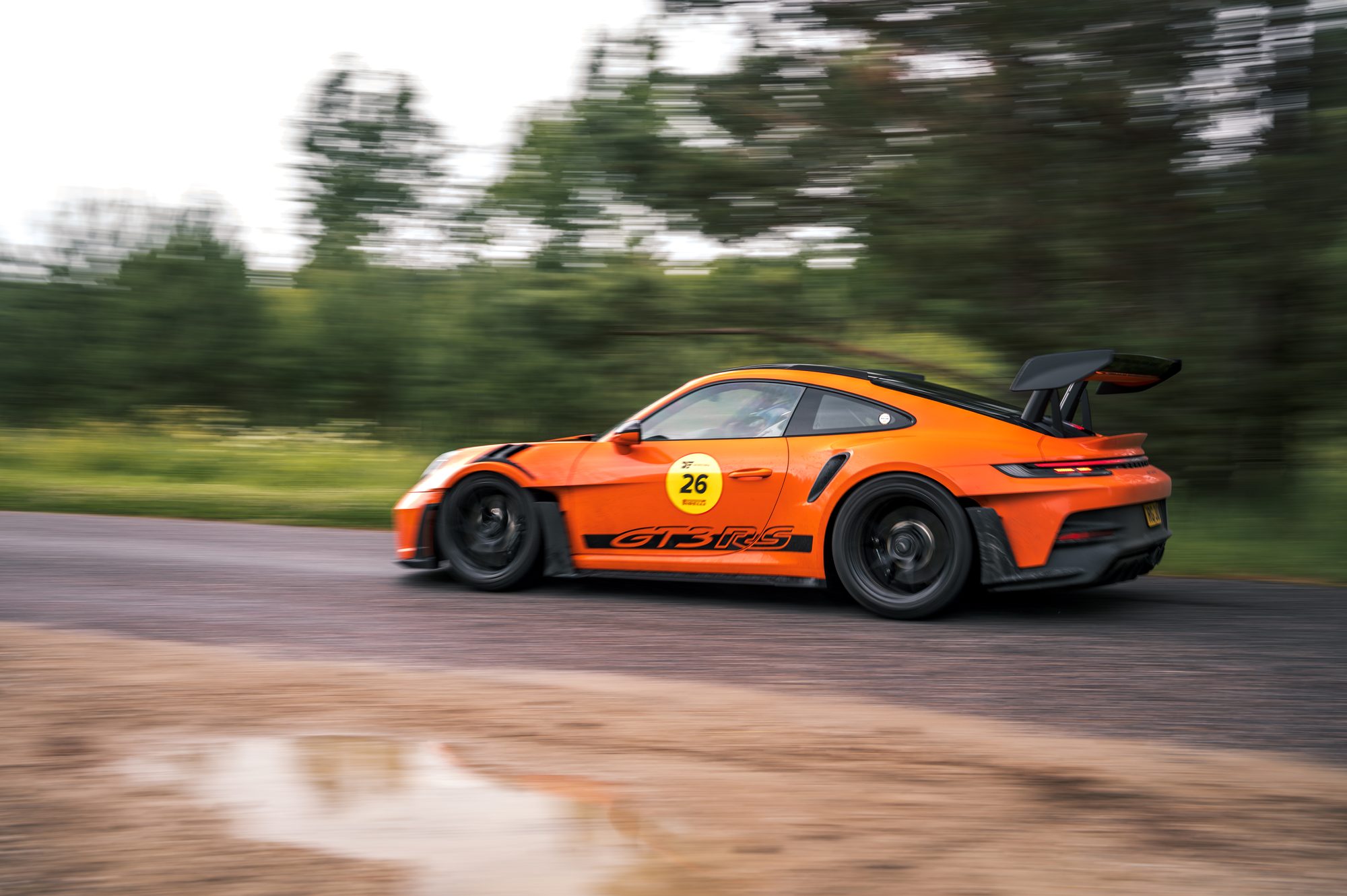 Orange Porsche 911 with a big rear wing, panning shot with the background streaked